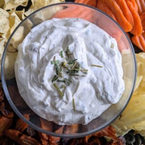 roasted garlic dip topped with chopped chives surrounded by chips and carrots