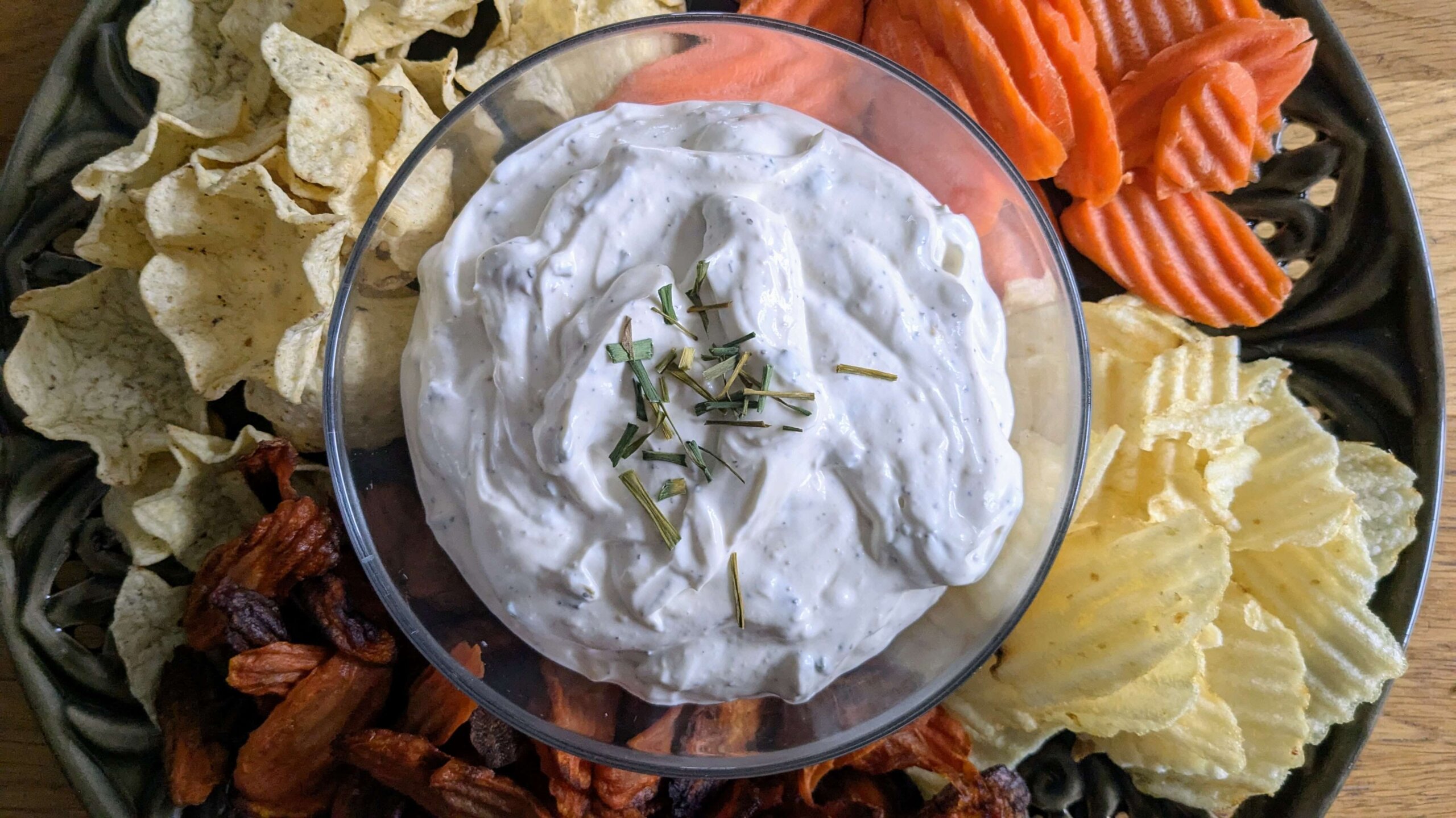 roasted garlic dip topped with chopped chives surrounded by chips and carrots