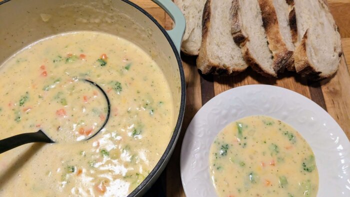 gluten-free broccoli cheddar soup in a Dutch oven being laddled into a white bowl next to slices of sourdough bread