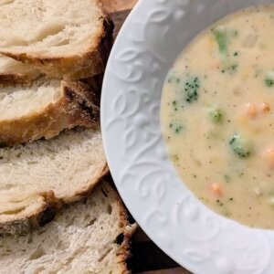 gluten-free broccoli cheddar soup in a white bowl next to slices of sourdough bread