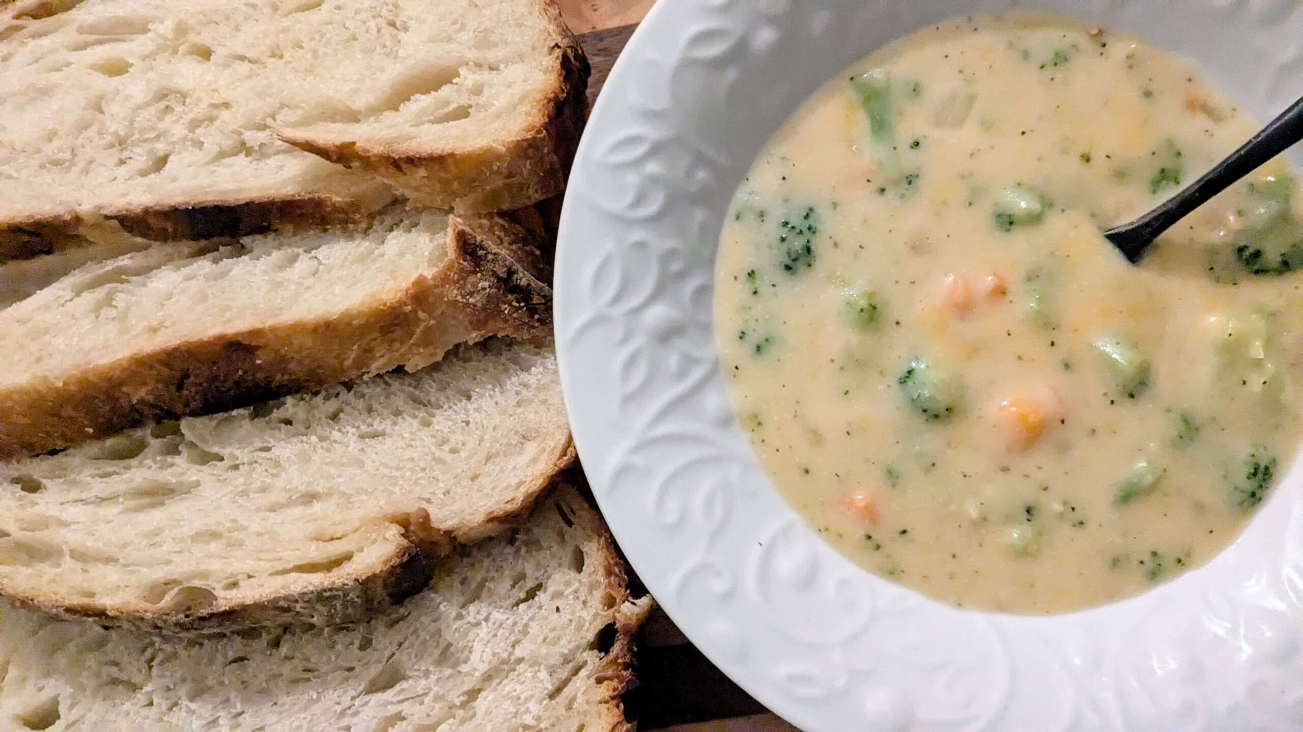 gluten-free broccoli cheddar soup in a white bowl next to slices of sourdough bread