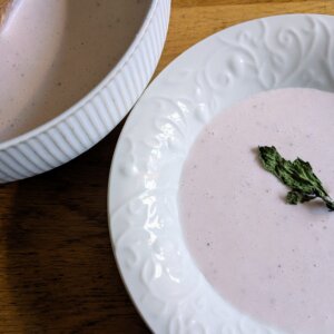 a bowl of strawberry bisque topped with dried mint, next to a serving dish of strawberry bisque