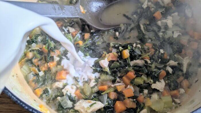 half and half being poured into a Dutch oven of chicken Florentine soup