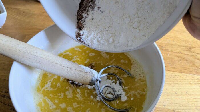 dry muffin batter ingredients being poured into a bowl of wet ingredients 