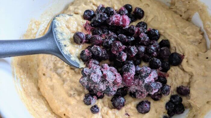 frozen blueberries sitting on top of batter with a black spatula