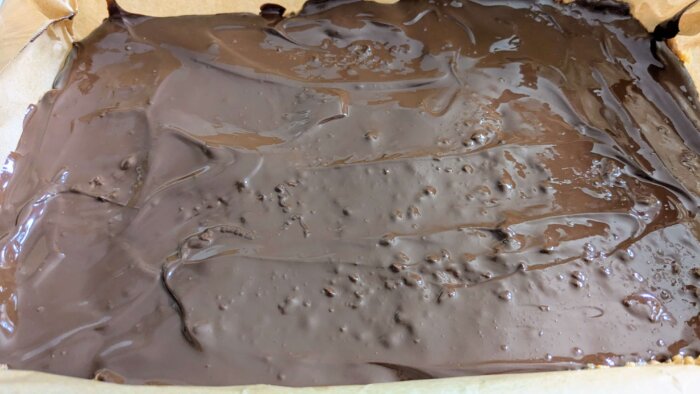 melted chocolate poured out evenly on a peanut butter and pretzel mixture