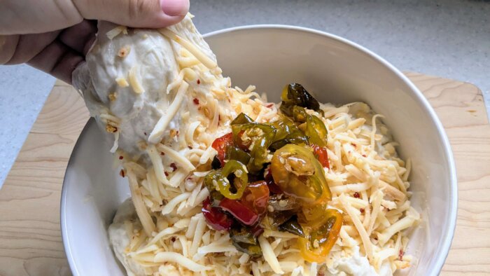 sourdough boule topped with shredded cheese and cowboy candy being stretched and folded