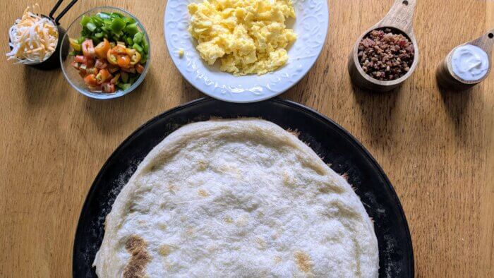 Pizza crust next to bowls of breakfast pizza toppings