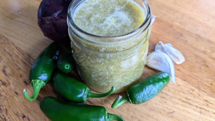 jalapeno Hot sauce in a small mason jar surrounded by jalapenos