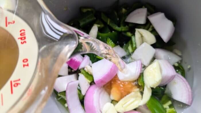 vinegar being poured into a pot with honey, salt, onions, garlic, and jalapenos