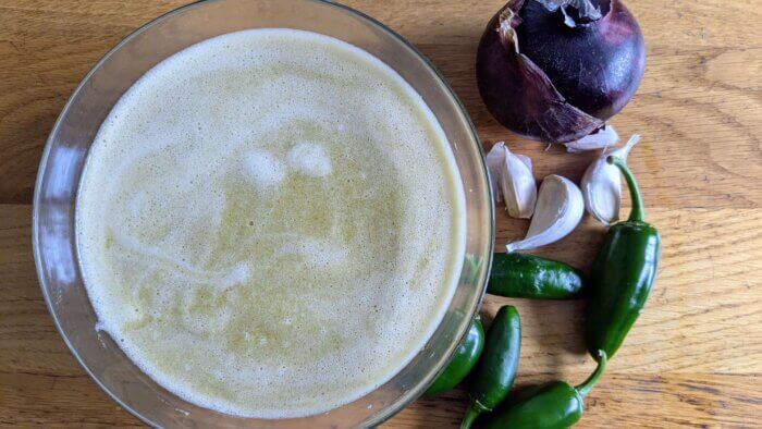 jalapeno Hot sauce in a bowl surrounded by jalapenos, garlic, and a red onion