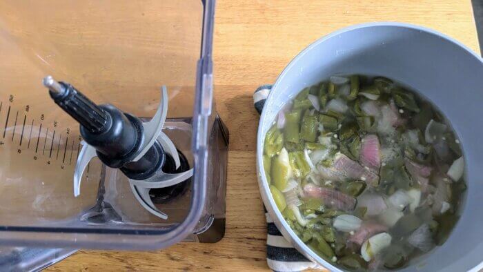 a blender next to a pot of cooked vinegar, honey, salt, onions, garlic, and jalapenos