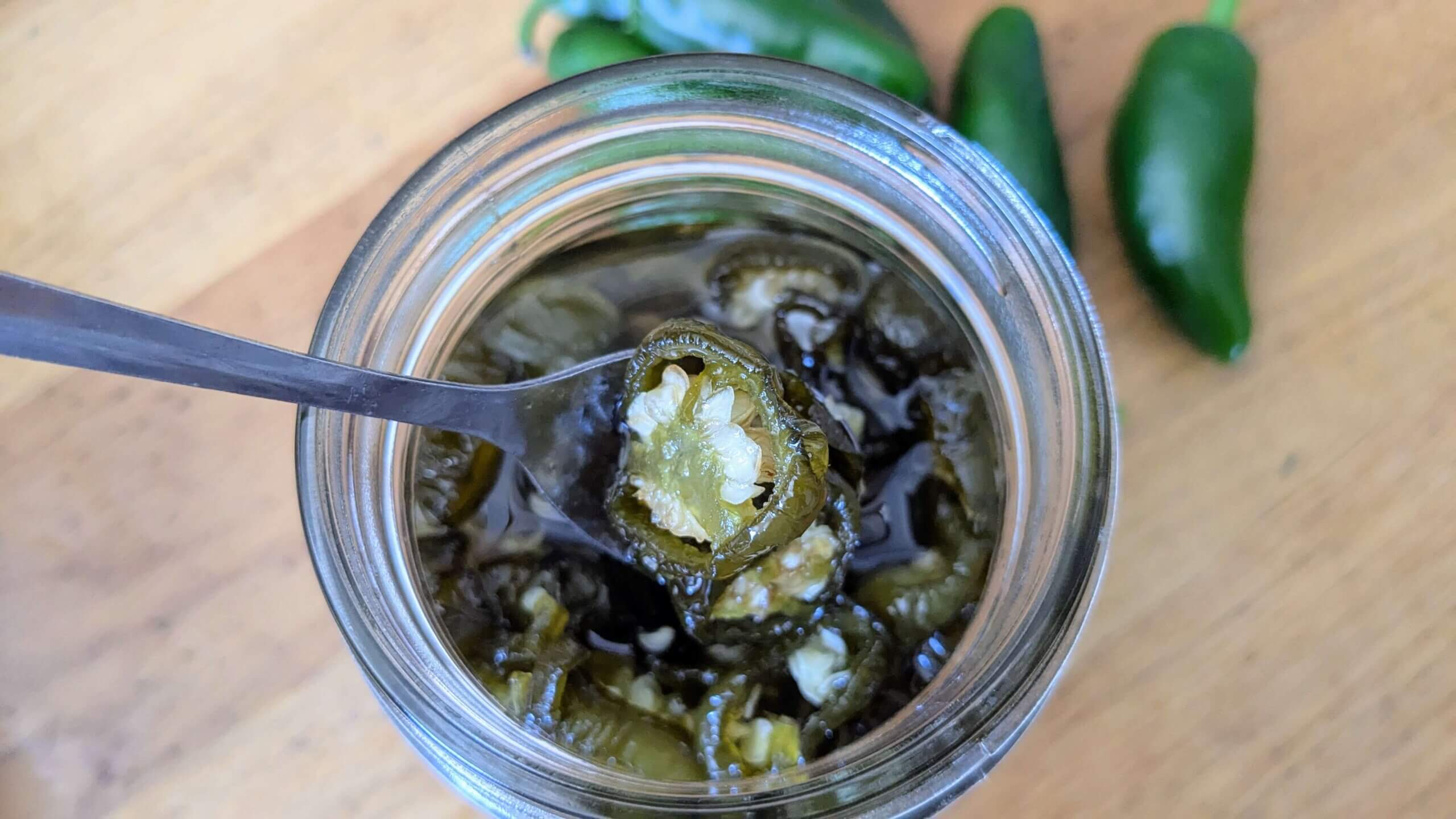 candied jalapenos in a jar with a spoon