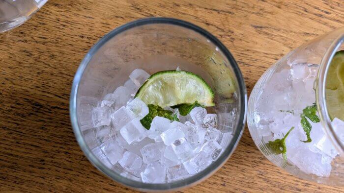 ice and mint leaves and lime wedges in two stemless wine glasses