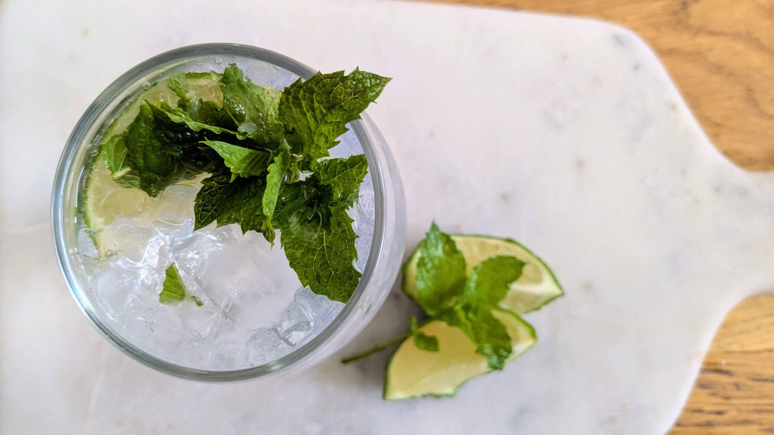 A stemless wine glass filled with a mojito mocktail on a marble cutting board next to a sliced lime and mint sprig