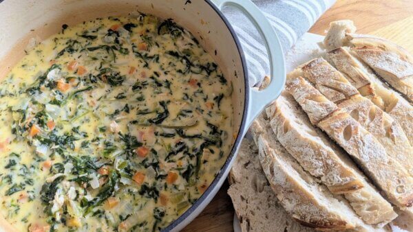 a Dutch oven full of chicken Florentine soup next to a loaf of sliced sourdough bread