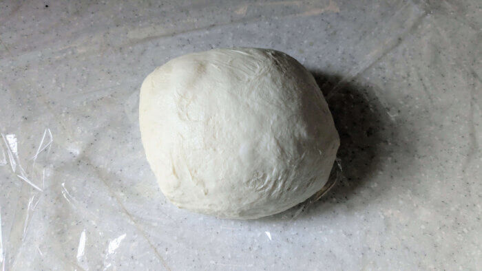 a ball of sourdough pizza dough on plastic wrap