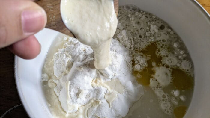 sourdough starter being poured into a bowl of flour, salt, oil, and water.