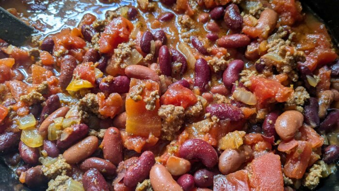 a crockpot filled with ground beef, onions, spices, beans, and tomatoes