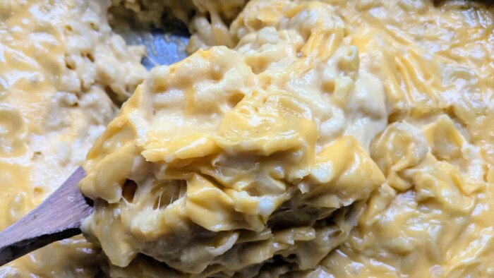 a wooden spoon scooping baked Mac and cheese out of a 9 x 13 pan.