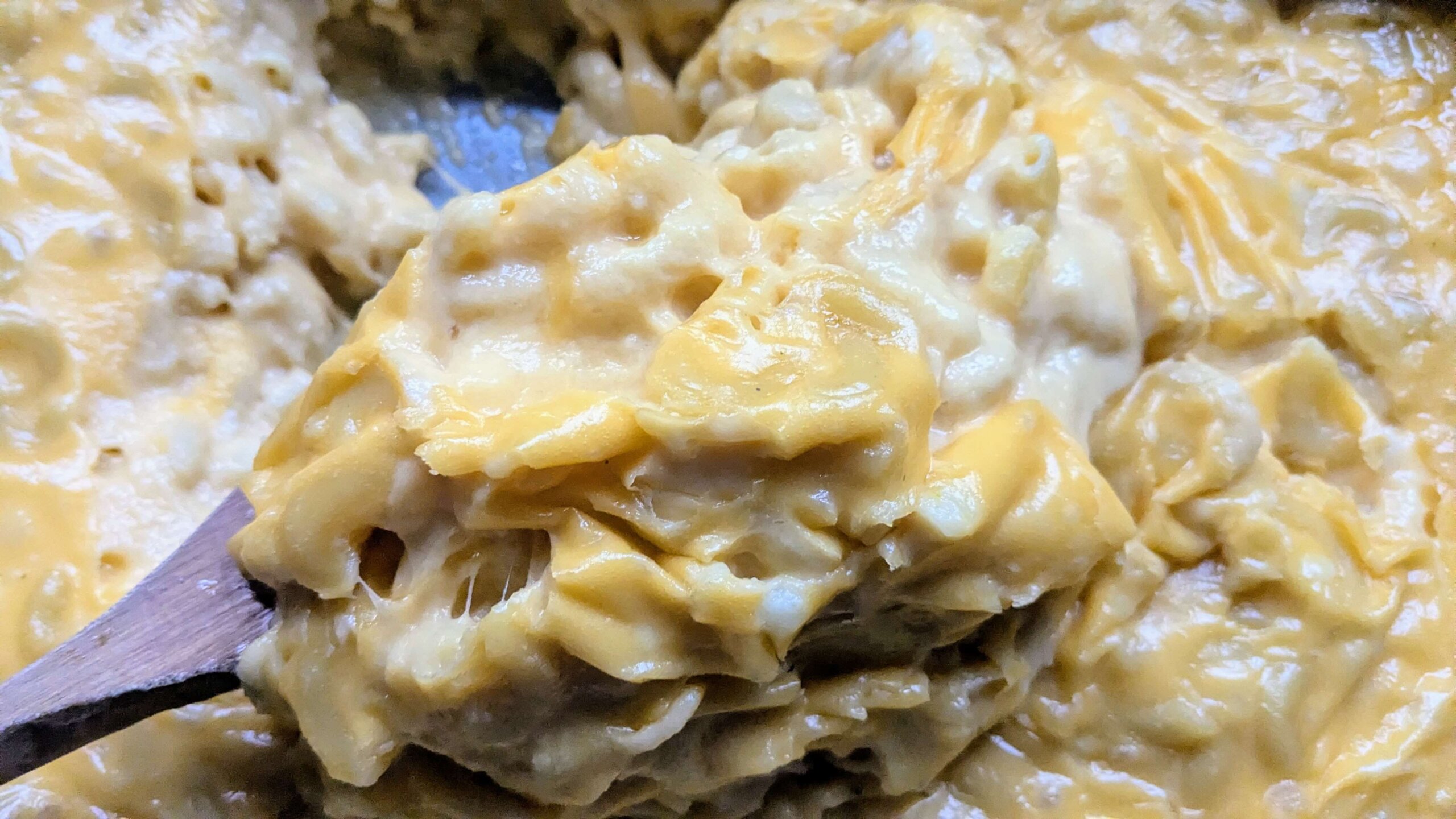 a wooden spoon scooping baked Mac and cheese out of a 9 x 13 pan.
