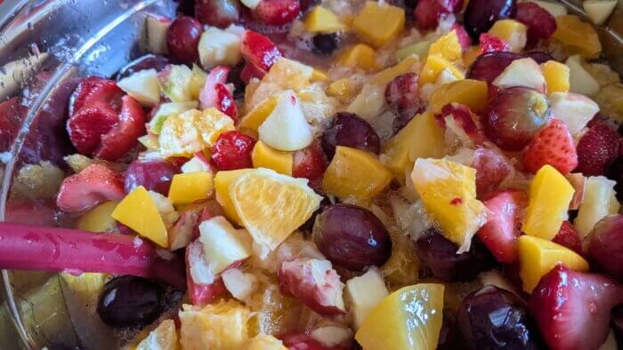 bowl of winter fruit salad mixed with a red spatula