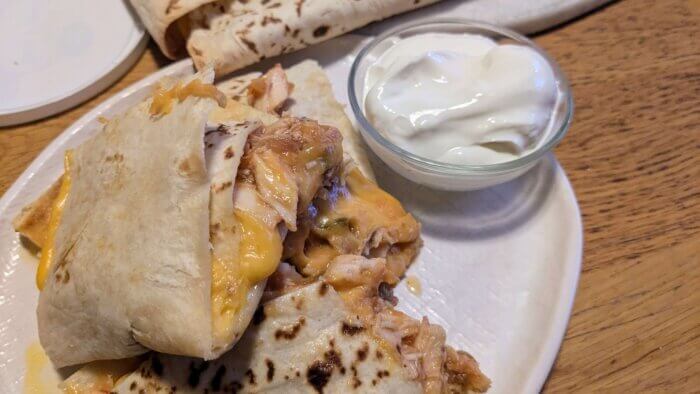 three chicken sheet pan quesadilla stacked on each other on a white plate next to a bowl of sour cream